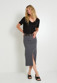 Haut noir à manches courtes avec col en V, associé à une jupe midi grise fendue sur le côté et une ceinture noire avec des accents dorés. Sandales noires à talons.