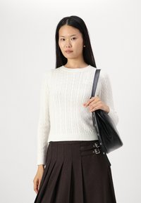 White cable-knit sweater with long sleeves, paired with a brown pleated skirt featuring silver buckle accents, and a black shoulder bag.