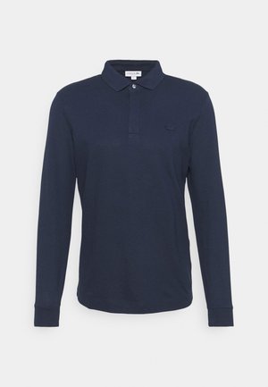 Tummansininen pitkähihaisen polo-paita puuvillasta, jossa on nappikaulus, ja rinnassa pieni brodeerattu logo sekä joustavat hihansuut.