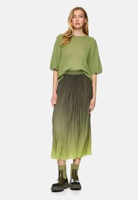 Green knit sweater with wide sleeves paired with a pleated skirt transitioning from dark green to light green, complemented by chunky black boots.