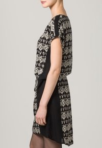 Abito a pois nero e crema, con maniche corte, vita aderente e una vestibilità ampia nella parte superiore, realizzato in tessuto leggero con motivi geometrici.