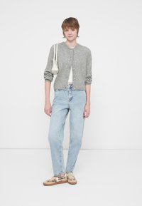 Cardigan cinza de malha com gola redonda, frente com botões e mangas longas, combinado com jeans de perna reta azul-claro e ténis estampados.