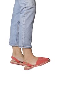Coral suede slingback sandals with an open toe, flat sole, and stitching details, worn with light blue cuffed jeans.
