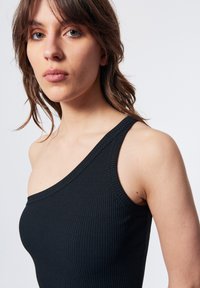 Top nero a righe con una spalla, dal design aderente, con una leggera texture e un ampio scollo. Primo piano che mostra i dettagli del collo e del busto.