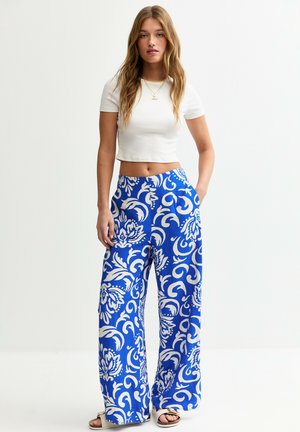 Wide-leg pants in bright blue fabric featuring a white floral pattern, with side pockets and a comfortable waistband. Paired with a cropped white top.