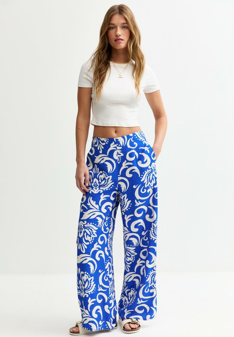 Pantalons à jambes larges en tissu bleu vif avec un motif floral blanc, dotés de poches latérales et d'une ceinture confortable. Associés à un haut blanc court.