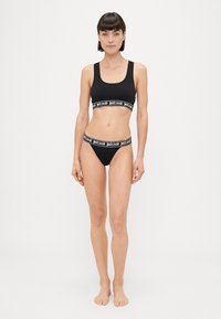 Crni pamukasti brus i bikini set s kontrastnim brendiranim elastičnim trakama. Jednostavan dizajn s glatkom teksturom i bez dodatnih uzoraka.