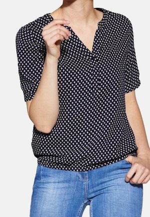 Marinebluse med hvidt diamantmønster, korte ærmer og V-udskæring. Materialet ser letvægtsagtigt ud med en afslappet pasform. Bæres med blå jeans.