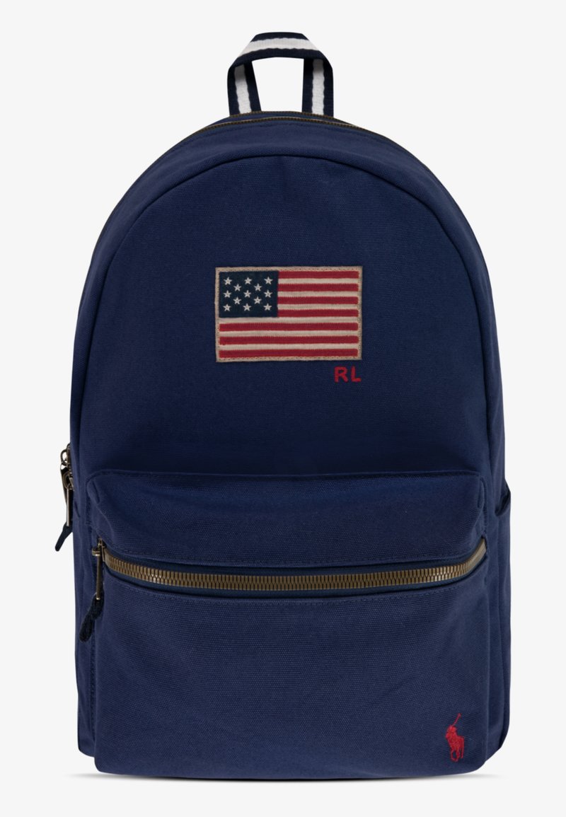 Marineblauwe canvas rugzak met een geborduurde Amerikaanse vlag, een voorzak met rits met gouden hardware en een kleine rode logo-accent.