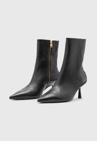 Botoșei de piele negri, până la glezna, cu vârful ascuțit, design elegant, detalii cu fermoar aurii și toc stiletto scurt. Textură netedă pe întreaga suprafață.