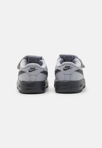 Sneakers Nike w szarym i czarnym designie, wykonane z materiału skórzanego, z płaskimi podeszwami i rzepem. Wyraźne logo znajduje się na pięcie.