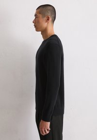 Zwarte trui van zacht materiaal, met lange mouwen en een ronde halslijn, gecombineerd met zwarte broek. Glad oppervlak, eenvoudig ontwerp.