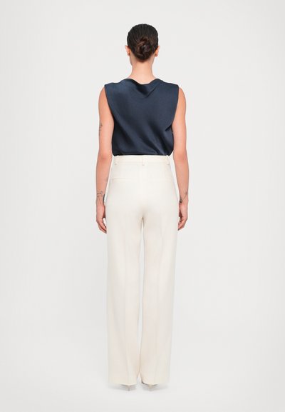 Navy satin sleeveless top paired with high-waisted, wide-leg, cream trousers featuring back pockets and a smooth finish.
