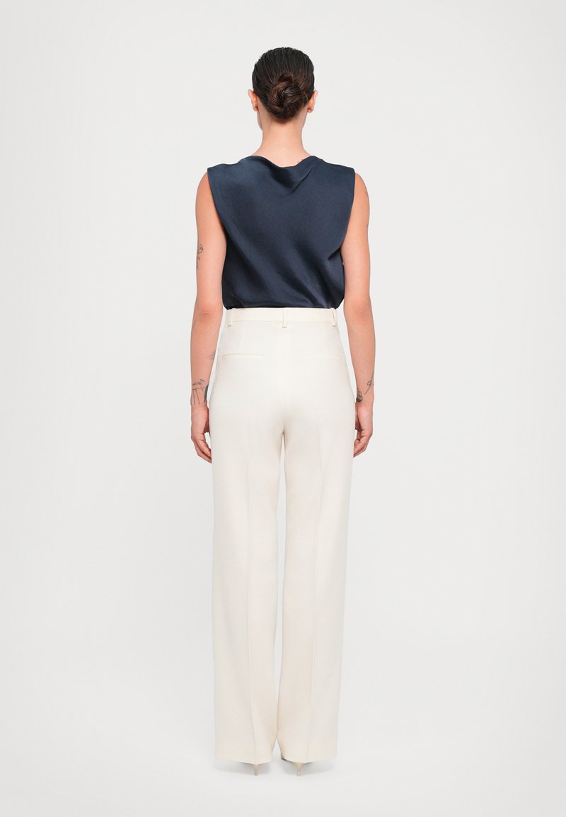 Navy satin ærmeløs top parret med højtaljede, brede bukser i cremefarve med baglommer og en glat finish.