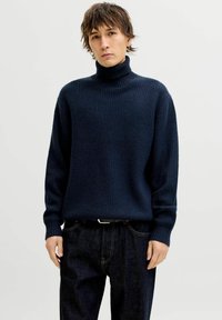 Marineblauer, gerippter Rollkragenpullover mit langen Ärmeln, ausgestattet mit einem strukturierten Strickmuster und einer lässigen Passform, kombiniert mit dunkelblauer Jeanshose.