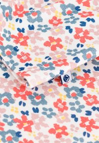 Tissu en coton floral de couleur blanche, présentant un motif coloré de fleurs rouges, bleues, roses et jaunes. Comprend une petite étiquette de marque.