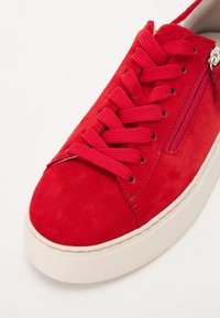 Baskets en daim rouge avec lacets larges et plats, fermeture éclair latérale et semelle épaisse en caoutchouc blanc, vues en angle de face.