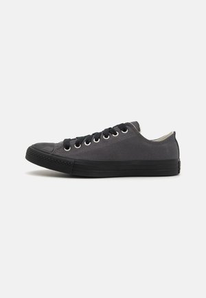 Sneaker basse en toile grise avec un embout en caoutchouc noir, des lacets noirs, des œillets en argent et une semelle en caoutchouc texturé.