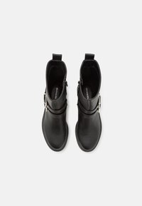 Botas de cuero negro hasta el tobillo con puntera redondeada, que cuentan con un zipper lateral, detalle de hebilla y una tira para tirar. Textura suave con un acabado mate.