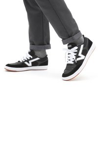 Svart og grå sneakers med hvite detaljer, med lavt design, snøring og en teksturert overflate, kombinert med grå bukser med oppbrett.