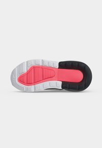 Sålen på en sneaker med hvid, pink og sort gummibane designet til greb og fleksibilitet.