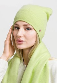 Berretto lavorato a maglia verde chiaro con risvolto e una piccola rifinitura metallica. Abbinato a una sciarpa verde chiaro coordinata, realizzata in materiale morbido.