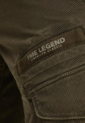 Dark green fabric with a textured pattern. Features a patch label with "PME Legend" and "American Classic" in silver lettering.