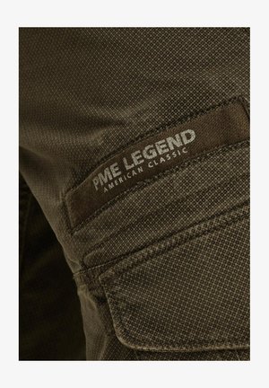 Temnozeleni material z teksturirano površino. Ima nalepko z oznako "PME Legend" in "American Classic" v srebrni barvi.