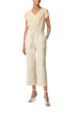 Top giallo a maniche corte con scollo a V; pantaloni larghi leggeri e fantasia con cintura da annodare; abbinato a sandali con tacco alto bianchi.