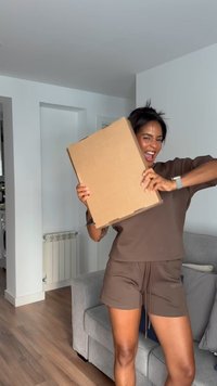 Une boîte en carton brun tenue contre une personne portant un haut à manches courtes et un short assortis de couleur brun, avec une texture lisse et une coupe décontractée.