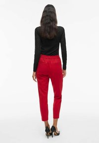 Pantalons rouges effilés avec une taille élastique, associés à un haut noir texturé à manches longues. Des chaussures à talons hauts noires complètent la tenue.