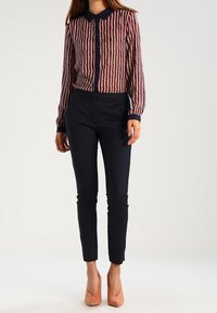 Camicia a maniche lunghe con colletto, a righe rosse e blu, abbinata a pantaloni blu aderenti e tacchi rosa chiaro.