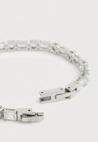 Ασημένιο μεταλλικό βραχιόλι με ορθογώνιες και τετράγωνες καθαρές κρύσταλλες, με κούμπωμα σημειωμένο "LIU.JO" για ασφαλή κλείσιμο.