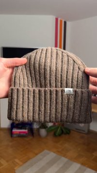 Brown ribbed knit beanie with a folded brim and a small white label, showcasing a textured fabric. Soft and warm appearance.