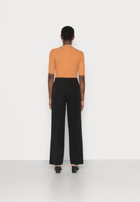 Top ajustado de cor ferrugem com mangas curtas, combinado com calças largas pretas de cintura alta. Tecido suave, design minimalista e linhas limpas.