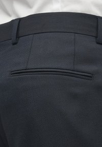 Jūras zila bikses ar teksturētu audumu, ar gludu jostu, aizmugurējo kabatu ar horizontālu flap, un elegantu piegriezumu.