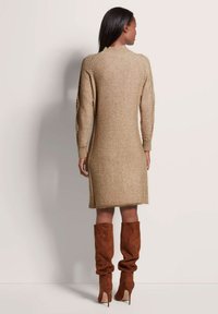 Gehaakte jurk in beige met lange mouwen, geribbelde manchetten en een hoge halslijn. Gecombineerd met bruine suède laarzen tot boven de knie. Glad textuur.