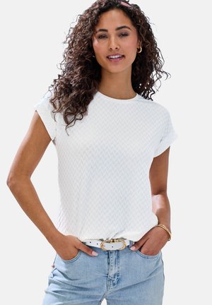 Camiseta blanca de manga corta con un patrón de chevron texturizado, combinada con jeans de color azul claro y un cinturón blanco con una hebilla dorada.