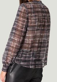 Blouse transparente à manches longues avec un motif à carreaux dans des teintes de violet foncé, noir et rose. Encolure froncée et poignets élastiques. Texture douce.