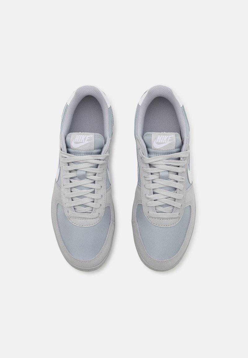 Hellgraue Sneaker aus einer Kombination von Wildleder und Mesh-Materialien, mit runder Zehenform, Schnürdesign und einem weißen Nike-Logo auf der Zunge.