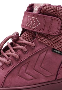 Vinröda höga sneakers med en texturerad tygkrage, en slät mockakropp och påtagliga chevron-accenter på sidorna. Justerbar rem ingår.