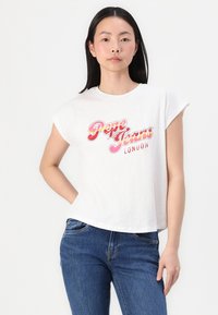 Balta medvilninė marškinė su sukrautomis rankovėmis, su spalvingu „Pepe Jeans London“ grafiniu atspaudu priekyje. Dėvima su mėlynomis džinsinėmis kelnėmis.