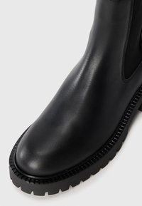 Bota de cuero negra hasta el tobillo con un acabado suave, punta redonda y suela de goma texturizada que presenta un diseño de banda de rodadura pronunciado.