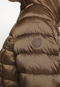 Bruine pufferjas met doorgestikt ontwerp. Zacht, glanzend materiaal met een cirkelvormig "Save the Duck" logo op de linker schouder.
