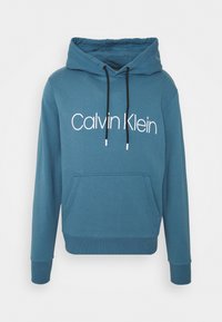 Niebieska bawełniana bluza z kapturem z kieszenią z przodu, regulowanymi sznurkami oraz wyraźnym białym logo "Calvin Klein" umieszczonym na klatce piersiowej.