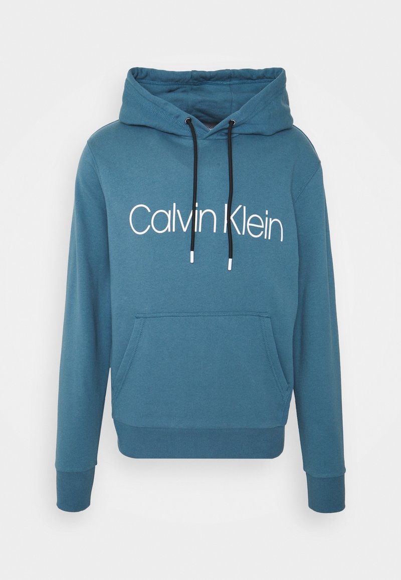 Niebieska bawełniana bluza z kapturem z kieszenią z przodu, regulowanymi sznurkami oraz wyraźnym białym logo "Calvin Klein" umieszczonym na klatce piersiowej.