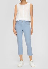 Blusa sin mangas blanca, jeans cortos azul claro y zapatillas blancas. Los jeans tienen un cierre de botón y cremallera, con bolsillos delanteros.