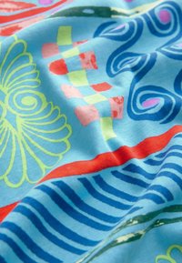 Barevný textil s světle modrým základem a abstraktními vzory v zelené, červené, růžové a tmavě modré, které zobrazují květinové a vlnité vzory.