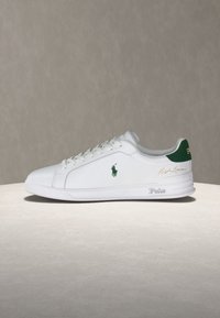 Λευκό sneaker χαμηλού ύψους με πράσινο λογότυπο Polo και πράσινη γλωττίδα στη φτέρνα, λευκά κορδόνια και το όνομα "Polo" εγχάραγμένο στη σόλα.