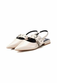 Zapatos slingback de charol beige con puntera afilada, una cinta con tachuelas y un pequeño tacón cuadrado. Presenta una hebilla decorativa de plata.